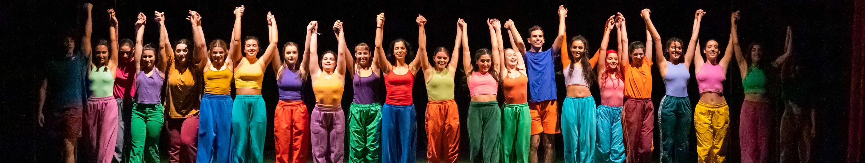 fila de bailarinos em palco com braços no ar 